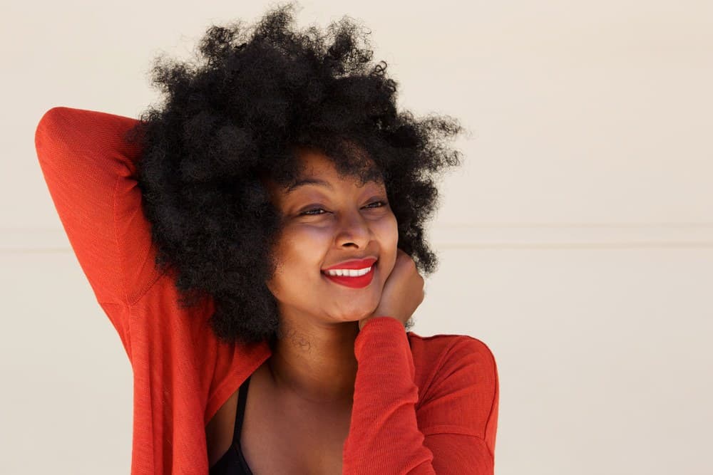 Pretty African American female with a curly afro create DIY spray products stored on the bathroom shelf