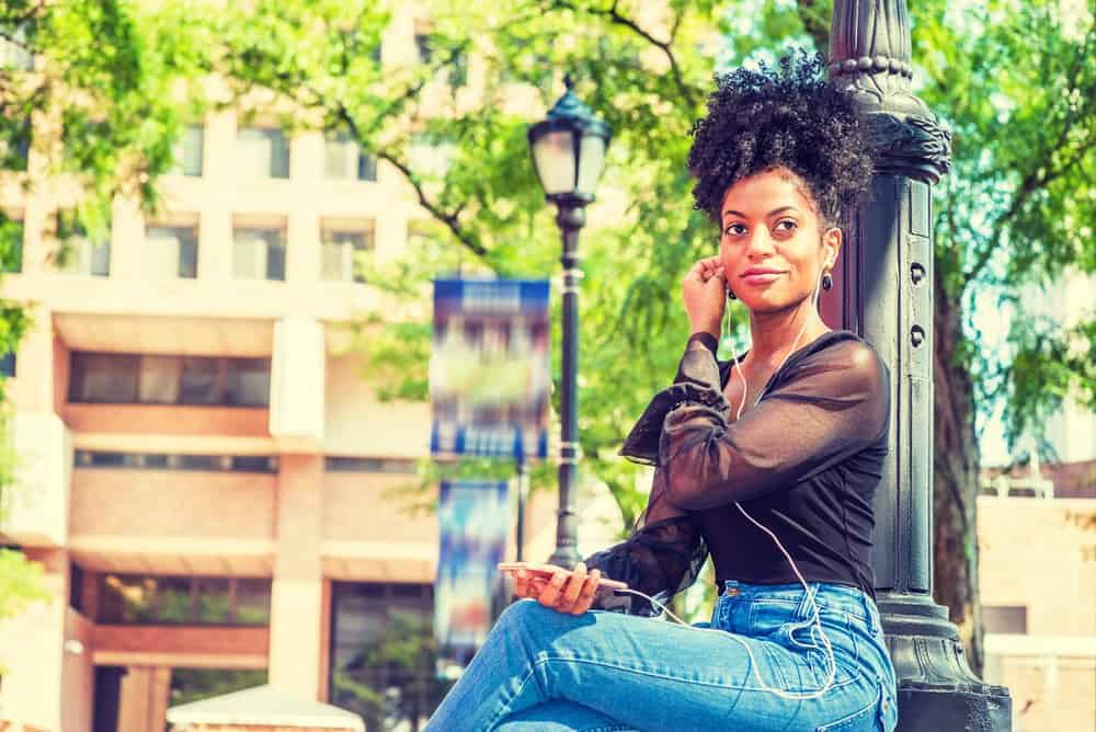 African American female sitting on park bench listen to Pandora music with iPhone headphones.