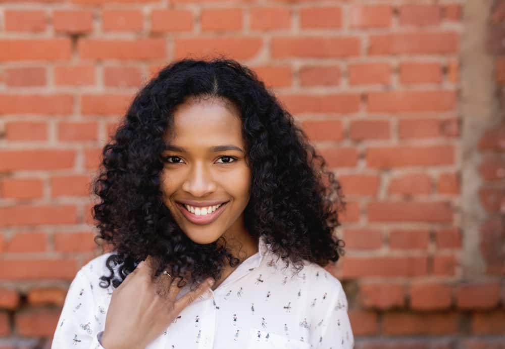 Female with a cute smile rubbing her hands through curly natural hair while wearing a white dress with a man riding a bike on the front. 