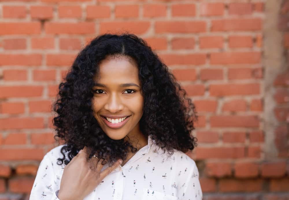 Female with a cute smile rubbing her hands through curly natural hair while wearing a white dress with a man riding a bike on the front.