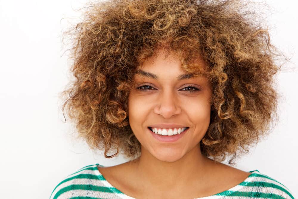 African American adult female with scalp irritation wearing a green and white sweater with type 3 b naturally curly hair