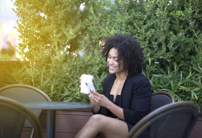 African American adult female wearing a black dress while sitting at an outdoor restaurant.