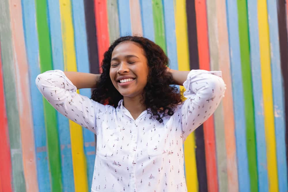 African American female with black hair rubbing her fingers through her curly hair strands with her eyes closed.