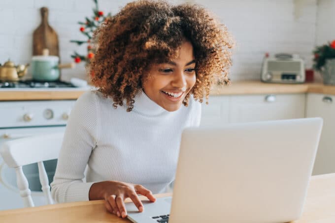 Young black girl using an Apple Macbook computer sitting in her kitchen.