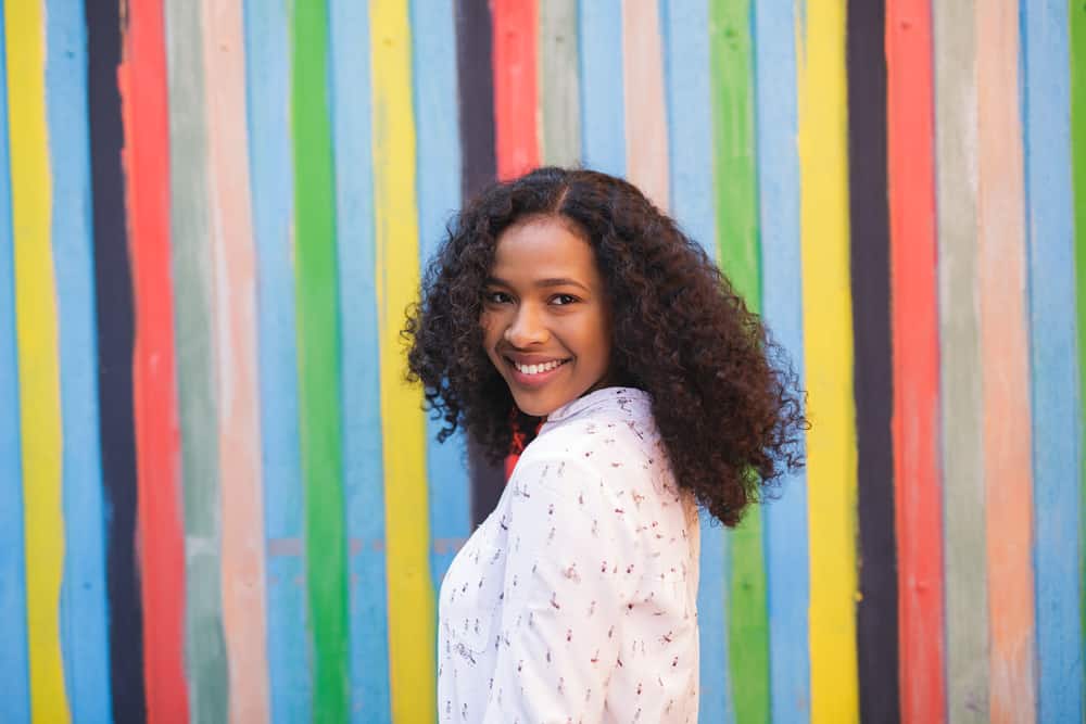 Women standing in a pageant pose smiling at the camera wearing a dress shirt with naturally curly hair.