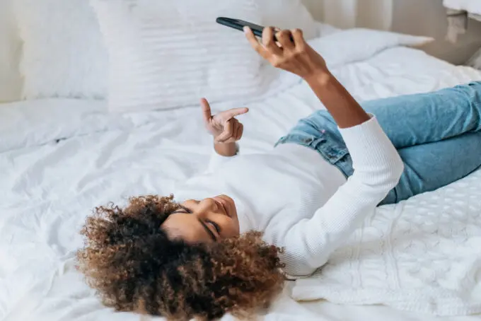 Black woman lying on the bed talking on an iPhone to a family member.