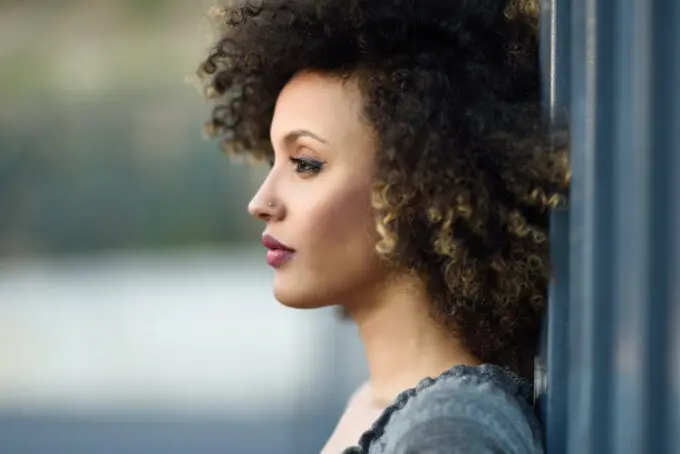 How To Dilute Hair Dye With Shampoo, Conditioner, Water, Pastel Colors, and More 4 American female with type 4B curly hair, a small nose ring, red lipstick while leaning up against the wall.