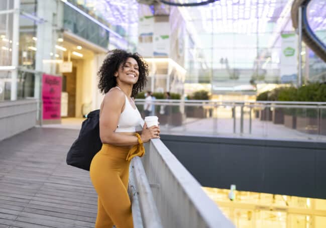 Lady with curly hair wearing a white shirt and orange pants at the mall.