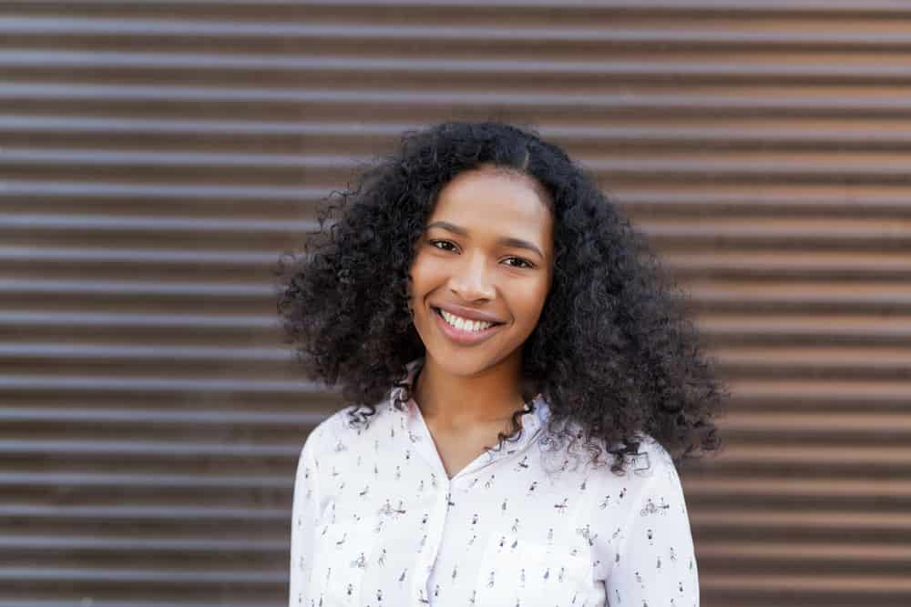 Black women leaning on a wooden barrier while smiling at the camera and holding the side of her face.