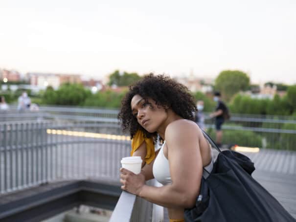 American female standing outside wearing workout gear, drinking a cup of coffee.