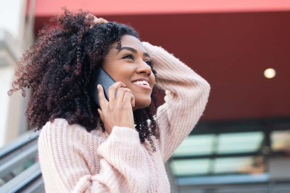 Women talking on a mobile phone wearing a finger coil hairdo created from her roots using the finger coil method.