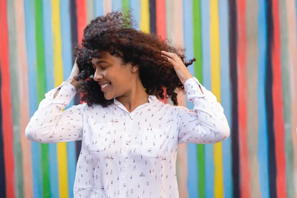 African American female with her eyes closed and turning her head quickly, making her naturally curly hair twist in the wind.