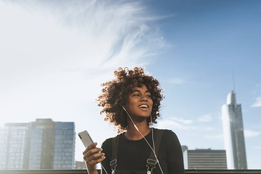 American female with type 3 curly hair using an iPhone 10 outdoors.