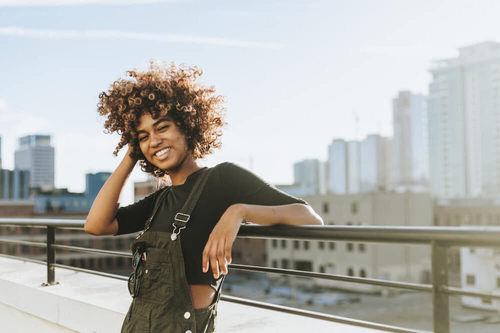 Beautiful African American female with curly hair treated with Triphala churna powder standing on a roof top.