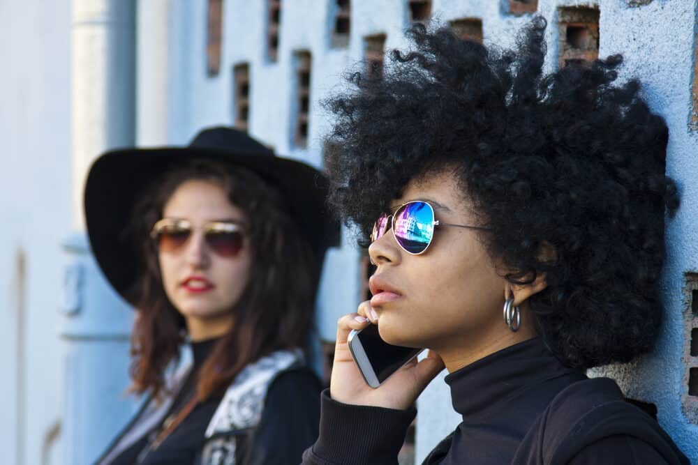 Young women standing beside a friend having a conversation on a mobile phone.