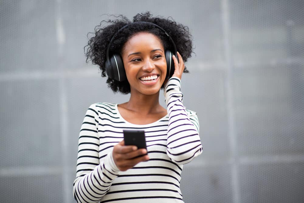 Beautiful black girl listening to wireless Beats Solo headphones paired with her iPhone 12.