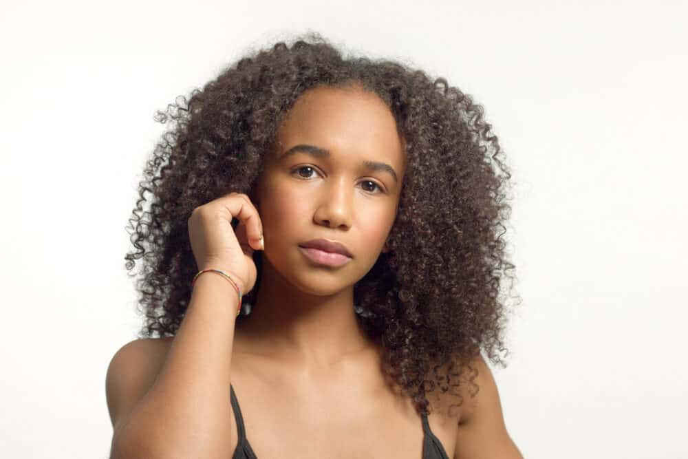 Woman with one hand at her cheek, her curls falling past her shoulders