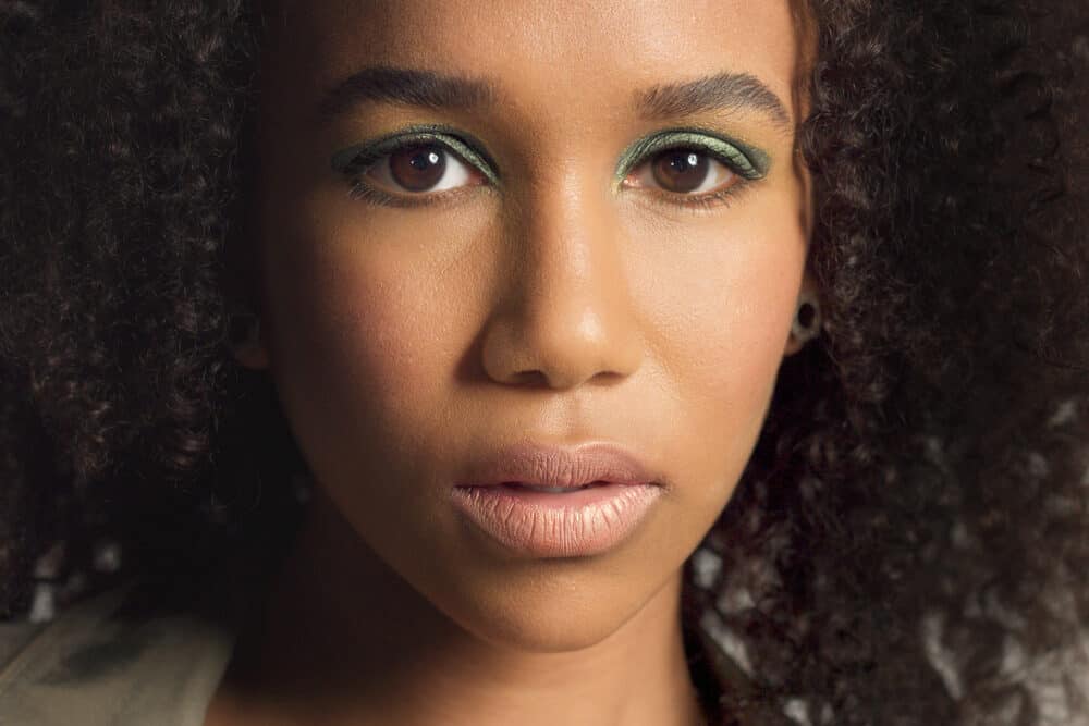 Close crop of the woman with green eyeshadow, her curls framing her face