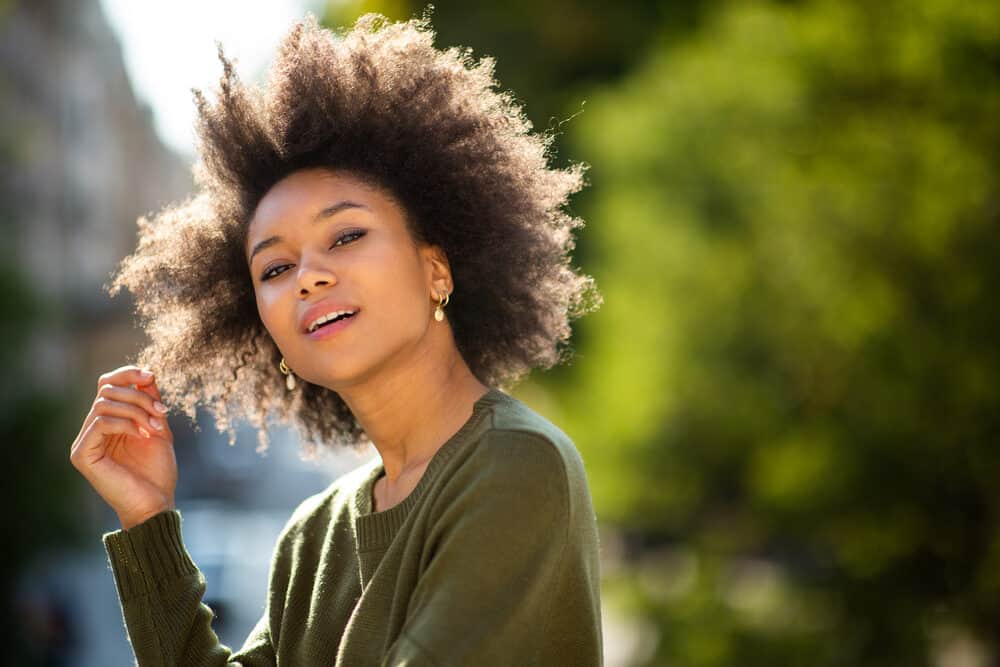 Cute black girl standing outside wearing a green sweater and gold earrings with curly hair.