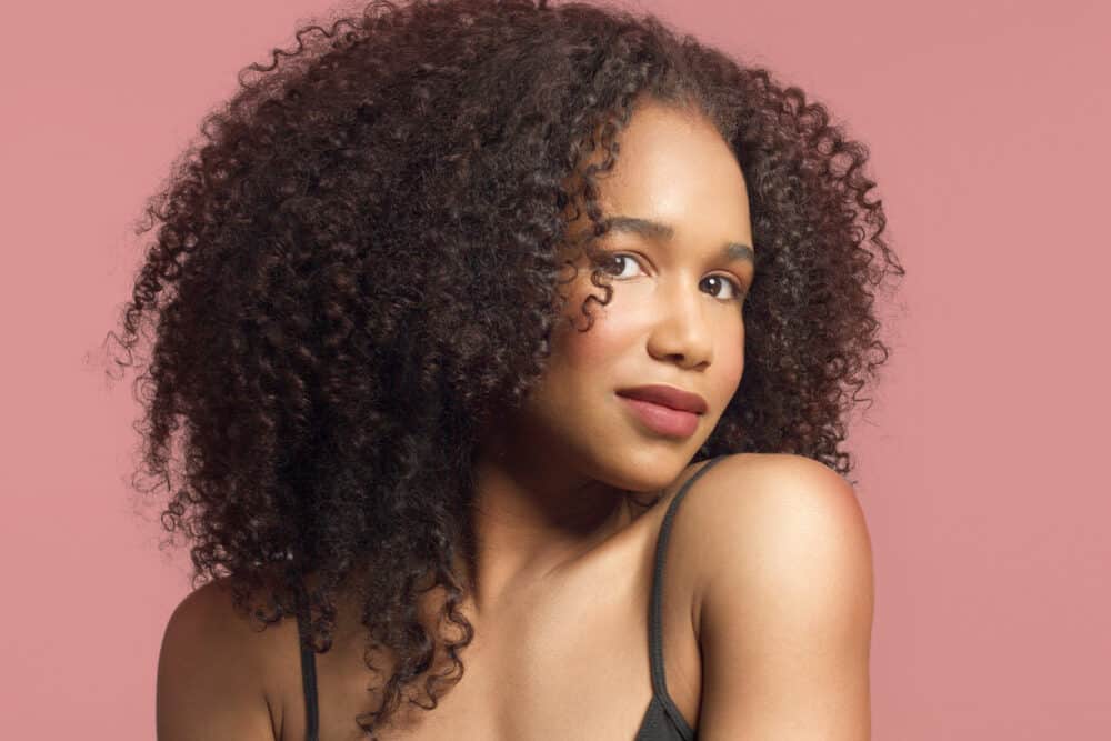 Woman against a pink backdrop, her curls full on both sides