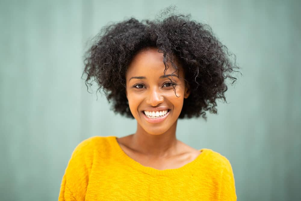 African American female after using bamboo tea for hair growth wearing a yellow sweater and pink lip gloss.