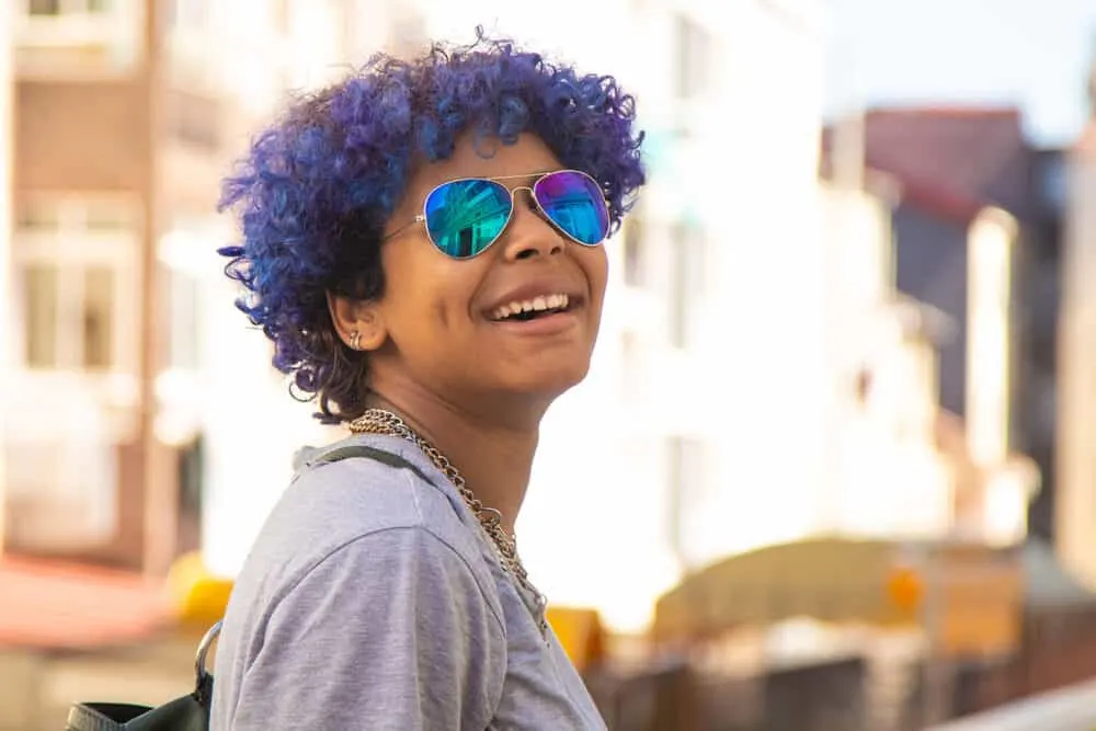 Hispanic female with blue hair looking back over her shoulder and smiling at the camera.