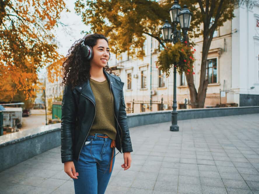 Cute Hispanic women with curly hair walking through the park while listening to music on headphones. 