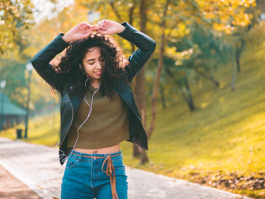 Cute Hispanic women dancing in the street while listening to rap music while leaves fall from the trees around her.