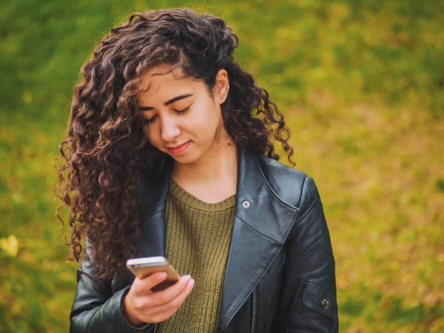 Young American woman sending a text message to her mom on an Apple iPhone 12.