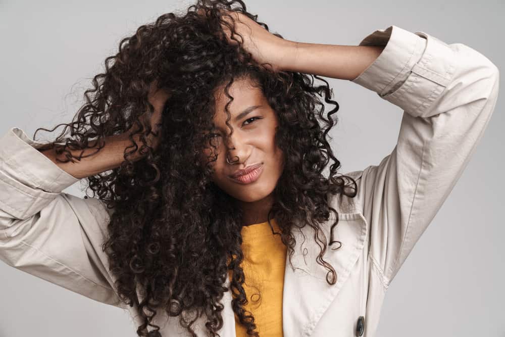 Attractive black woman with type 3 curly hair wearing a winter jacket rubbing her hands through her natural hair.