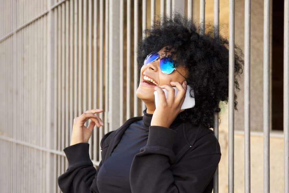 Woman leaning up against a fence, talking on a mobile phone, while laughing at her friend's joke.