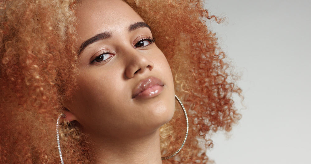 Lady with reddish blonde naturally curly hair with a frizzy texture wearing pink lipstick and a blue suit