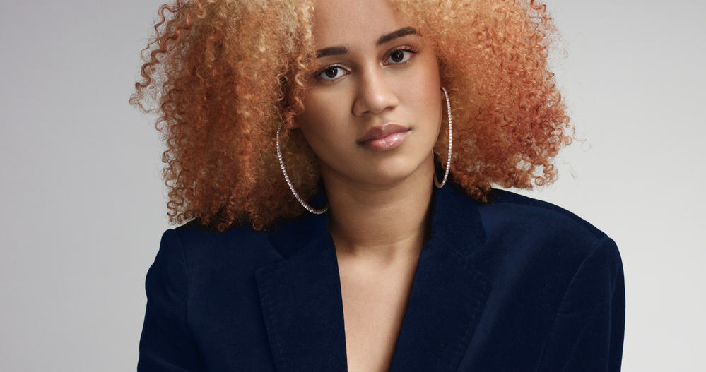 Cute mixed-race lady with curly afro and diamond hoop earrings wearing a blue business suit