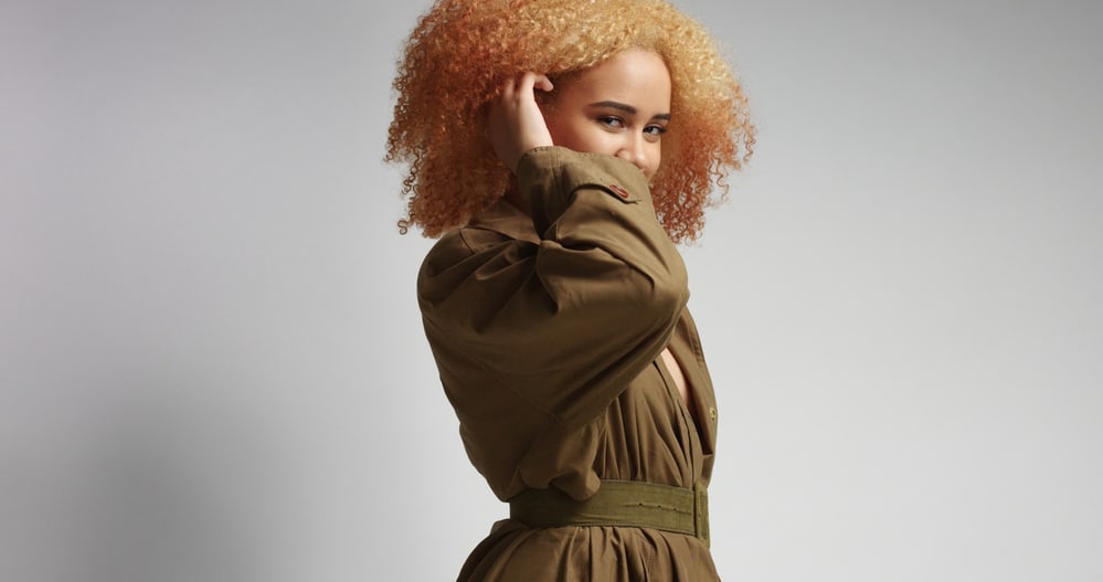 Lady rubbing her hair with a green khaki coat with a belt around her waist 