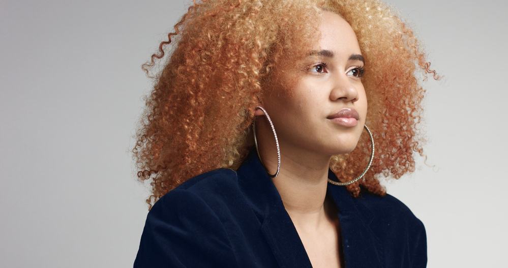 Black female with curly hair that been treated with bleach powder and liquid ammonia wearing a blue jacket