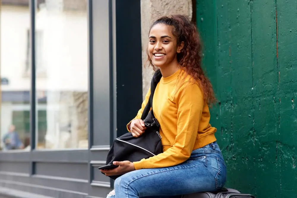 Should You Wash Your Hair Before a Haircut or Before You Color It? 7 Indian girl ready to travel with a duffle bag, sweatshirt, and torn blue jeans
