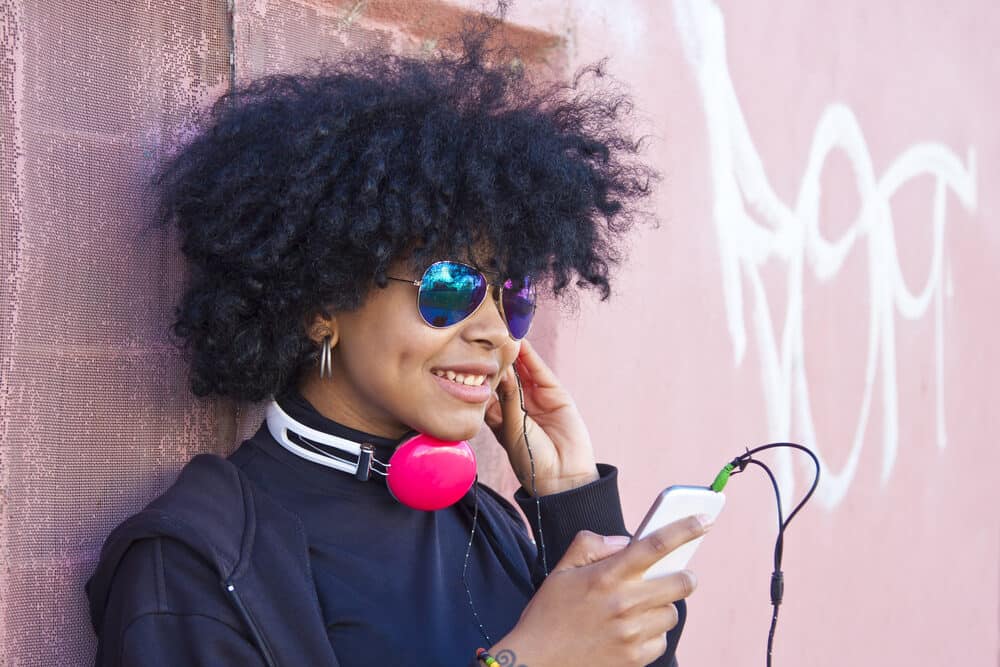 Black women standing outside having a hard time hearing her music on broken earphones.