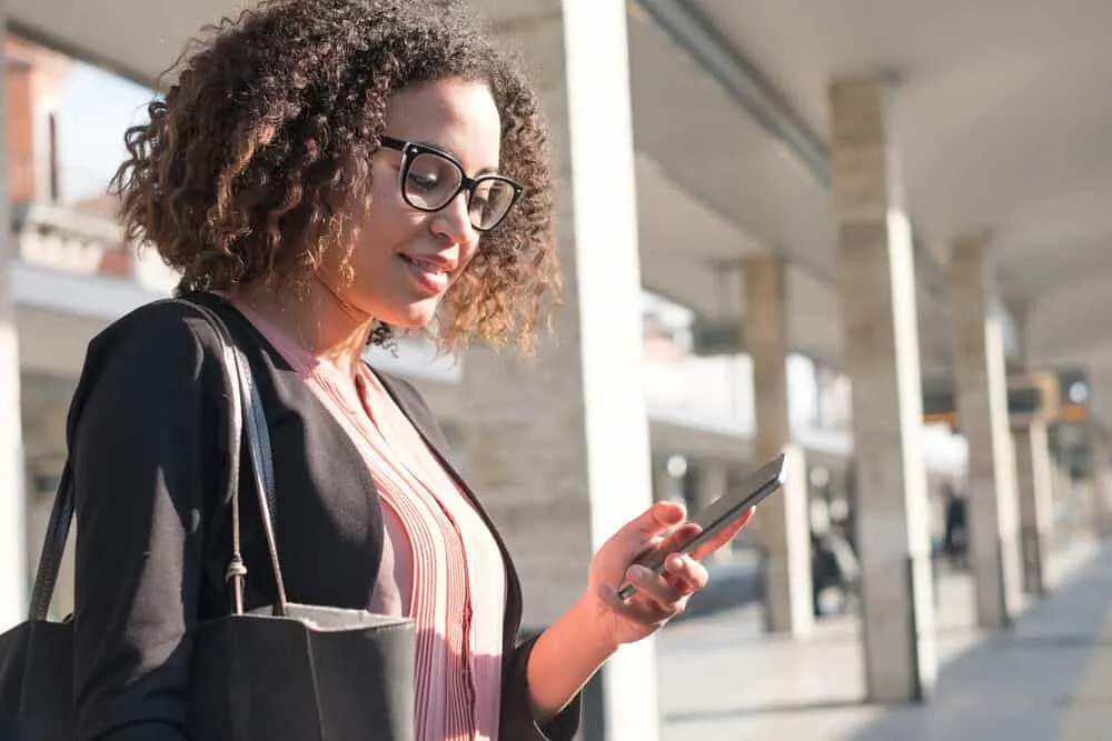 How Long Does It Take To Get Highlights Done in Your Hair at a Salon? 7 Lady standing outside using a cell phone at the subway with curly type 3c hair strands.