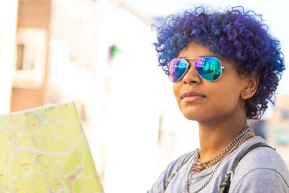 How to Dye Dark Hair Purple With and Without Bleach at Home 5 Female wearing rainbow shades, purple-blue hair, earrings, and natural lipstick color.