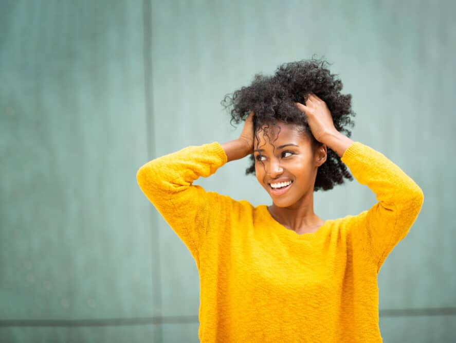 Black woman rubbing her naturally curly hair outside during a photo session.