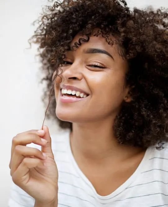 Beautiful young African American woman smiling at the camera with curly hair after using chebe powder for hair growth and length retention.