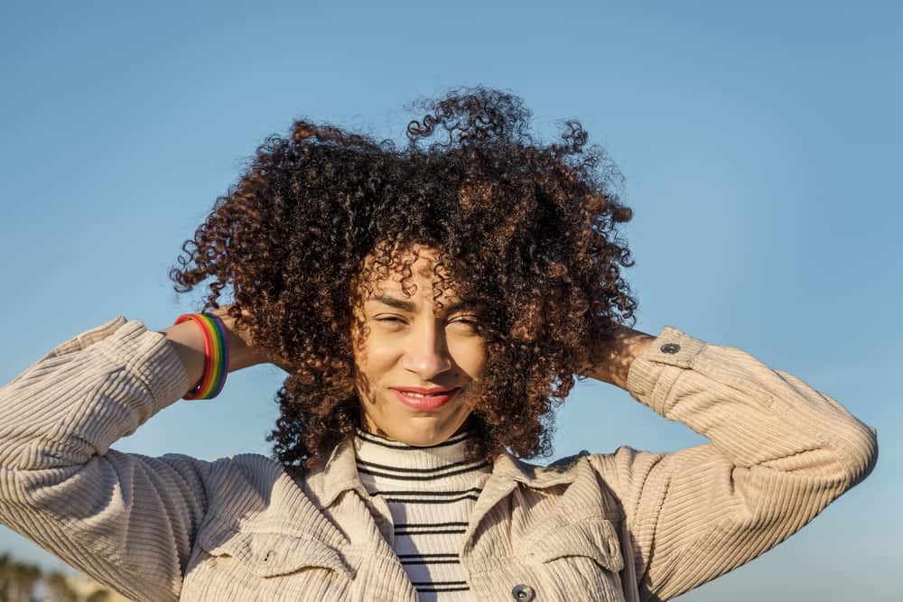 Young black woman with naturally curly hair wearing a rainbow bracelet that has used rosehip oil for scalp health, collagen production, and a dry scalp condition.