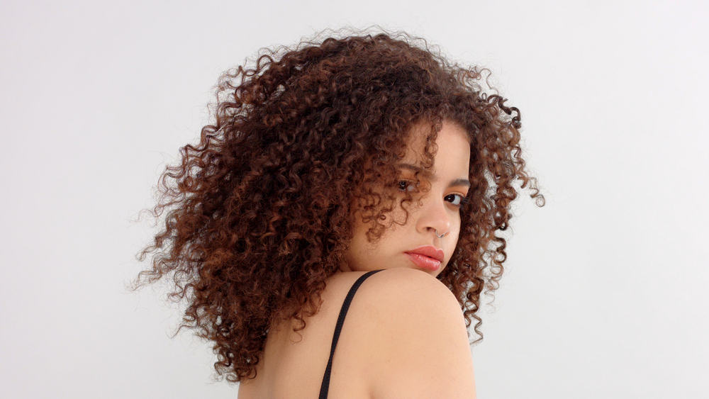 Mixed-race female looking back over her shoulder into the camera with red lipstick and type 3c curls.
