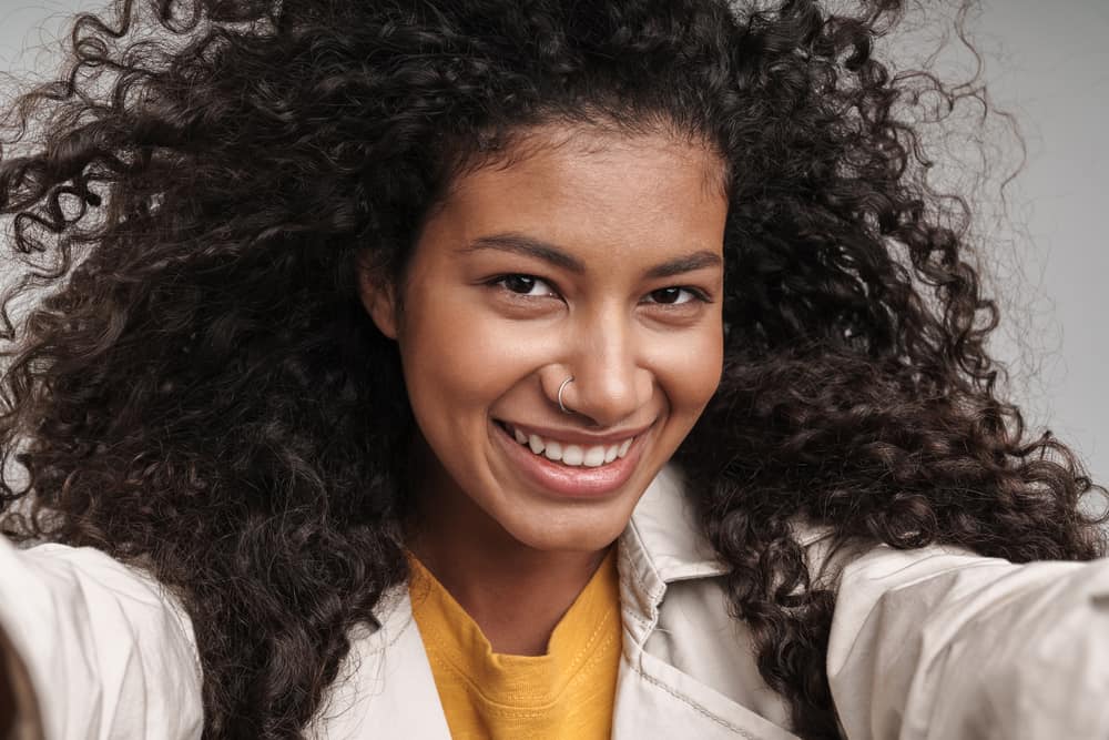 African American female with naturally curly hair that's been treated with jasmine oil for hair growth posing in front on a blue background.