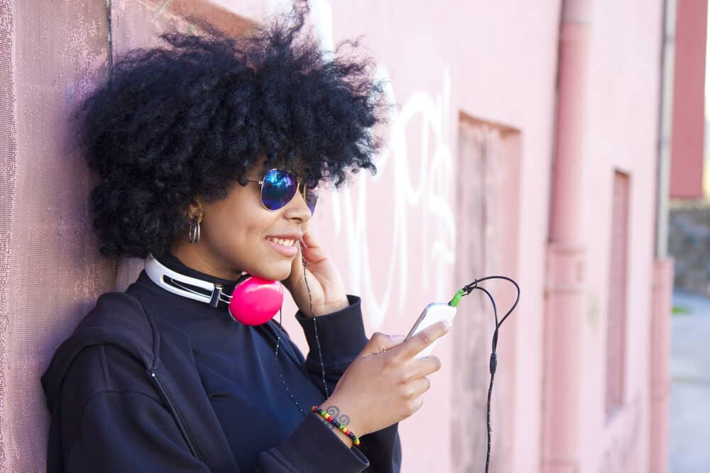 Pretty black female with tight curls wearing a black shirt, dark jacket, and hoop earrings.