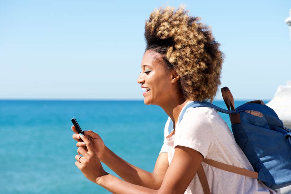 African American women with braided type 4c hair strands using a mobile phone on a boat.