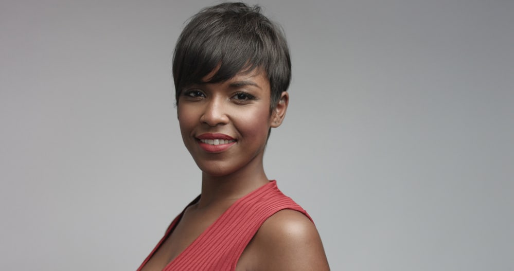 Black adult female with straight hair wearing make-up and stylish red dress looking into the camera while smiling.