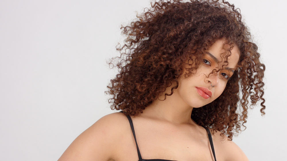 Adult female wearing a black spaghetti strap tank top and ombre curls with highlights.