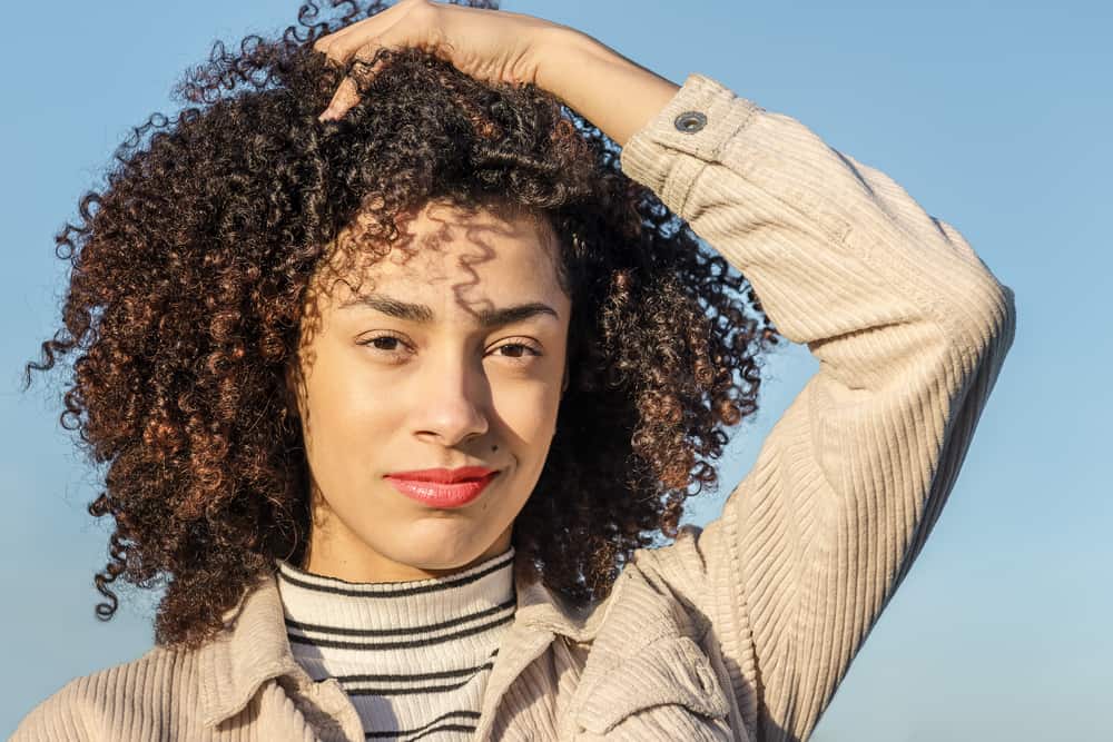 Young black girl with a pretty smile rubbing her fingers through her naturally curly hairdo that's been treated with cold-pressed rosehip oil.