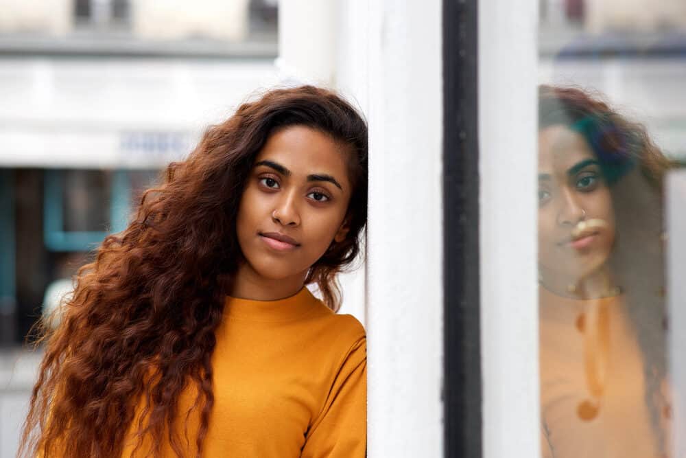 Indian American woman with long brown hair leaning against wall